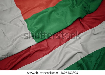 waving colorful flag of hungary and national flag of madagascar. macro