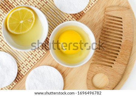 Raw egg in the small white bowl, wooden hair brush, lemon juice with lemon slice. Natural homemade hair treatment and zero waste concept. Top view, copy space