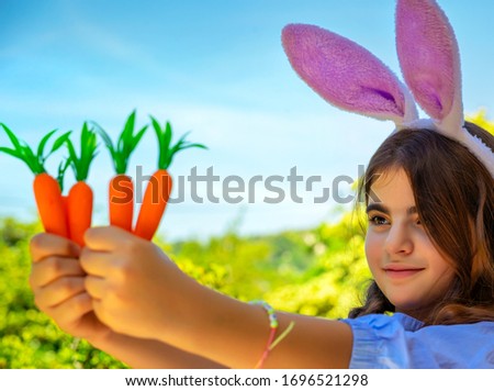 Portrait of a sweet little girl dressed as bunny playing with carrots, gardening and having fun outdoors in sunny spring day, Easter celebration outdoors
