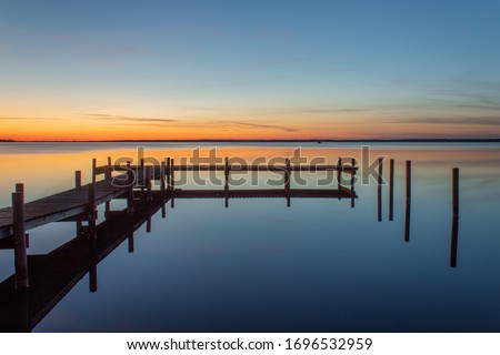 Warm sunset at the sea with a jetty and reflections in the water. Boundless widths, colorful gradients give a harmonious feeling. Very colourful with orangs and red sky colors and blue like the sea.