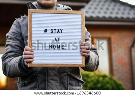 Man holding in his hands letter box with words "Stay at home", on the background of house.