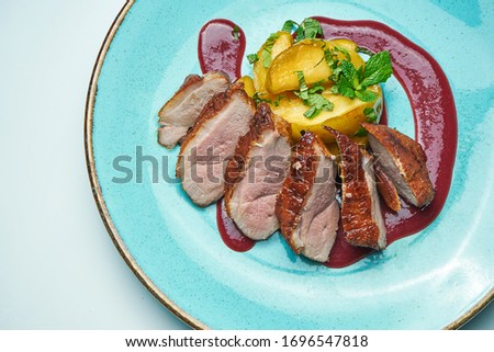 Appetizing baked sliced duck fillet with berry sauce and apples on a blue plate isolated on grey background. Close up.