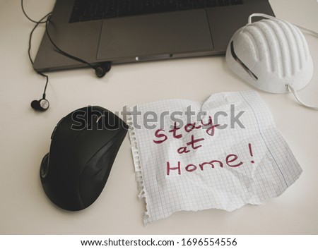 A laptop, respiratory mask, headphones and a paper with words "Stay at home" .Concept of self quarantine at home as preventative measure against Coronavirus.