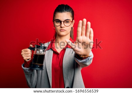 Young beautiful brunette woman doing coffe holding french coffeemaker over red background with open hand doing stop sign with serious and confident expression, defense gesture