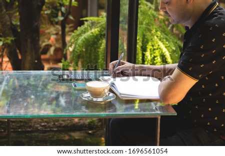 Pakistani business asian man in casual wearing casual write on notebook using smart mobile phone with cup of coffee in cafe,freelance business concept.