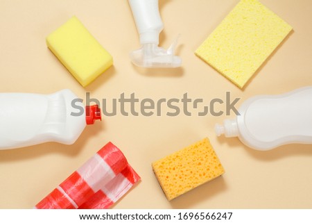 Plastic bottles of dishwashing liquid, glass and tile cleaner, detergent for microwave ovens and stoves, garbage bags and sponges on a beige background. Top view. Washing and cleaning set.