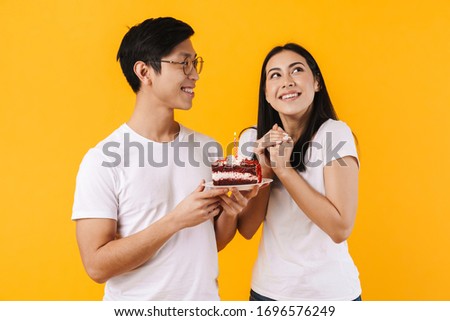 Image of happy multinational couple holding cake with candle while celebrating birthday isolated over yellow background