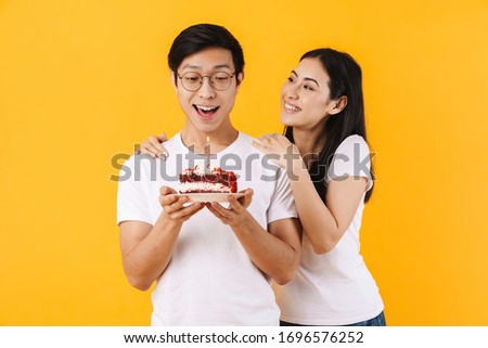 Image of happy multinational couple holding cake with candle while celebrating birthday isolated over yellow background