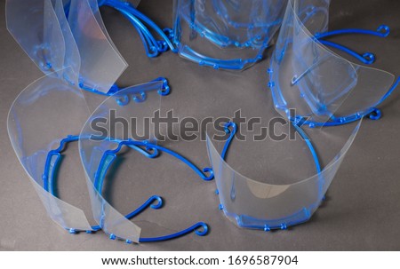 A number of 3d printed face shields, completed assembly with transparent plastic attached to blue pla visor.  Home made PPE ready for donation to health care workers during the COVID-19 pandemic. Royalty-Free Stock Photo #1696587904
