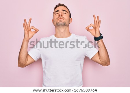 Handsome man with blue eyes wearing casual white t-shirt standing over pink background relax and smiling with eyes closed doing meditation gesture with fingers. Yoga concept.