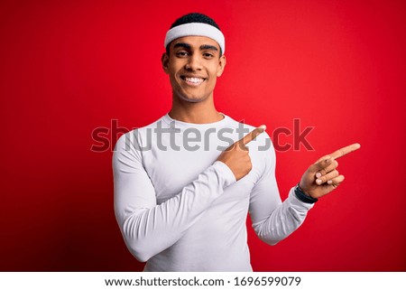 Young handsome african american sportsman wearing sportswear over red background smiling and looking at the camera pointing with two hands and fingers to the side.