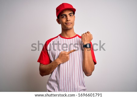 Young handsome african american sportsman wearing striped baseball t-shirt and cap In hurry pointing to watch time, impatience, looking at the camera with relaxed expression
