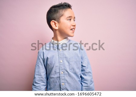Young little boy kid wearing elegant shirt standing over pink isolated background looking away to side with smile on face, natural expression. Laughing confident.