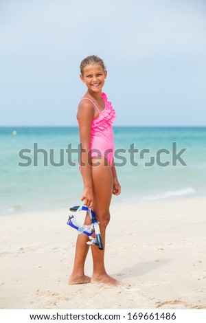 Cute girl on beach with blue face masks and snorkels, sea in background.