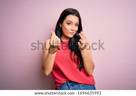Young brunette woman wearing casual summer shirt over pink isolated background doing money gesture with hands, asking for salary payment, millionaire business
