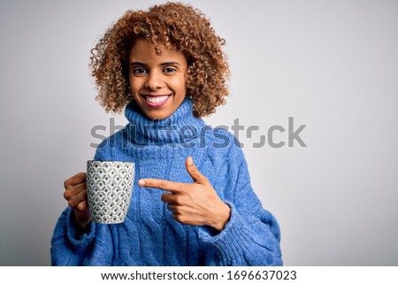 Young african american curly woman drinking mug of coffee over isolated white background very happy pointing with hand and finger