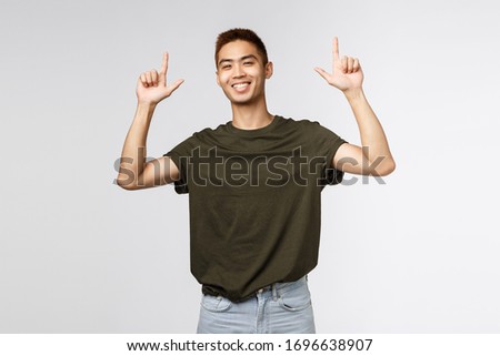 Portrait of proud happy, smiling asian young man, teen guy pointing fingers up and grinning at camera satisfied, person showing way to promo, advertise product or company banner