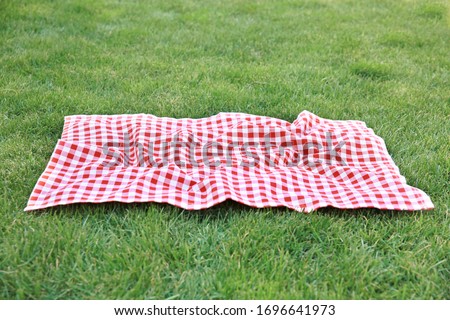 Red picnic blanket on green grass background,empty space gingham tablecloth outdoors food advertisement design.Easter decorative backdrop. Royalty-Free Stock Photo #1696641973