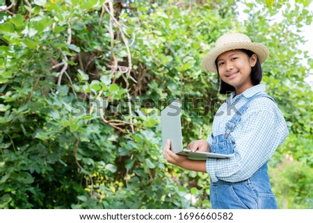 Young girl using a notebook computer in the front garden with a bright smile. She has ideas for nature conservation and research on tree and plant species. Concept of environmental conservationists.