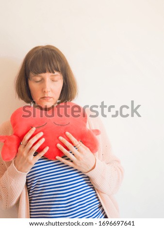 Young woman wearing striped t-shirt hugging red heart shaped plush toy