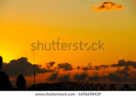 Wide shot of an airplane landing with a warm sunset with flashes of light in the background