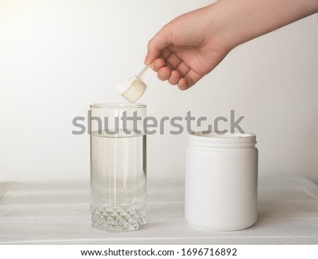 hand holding scoop of fish collagen. collagen peptides in container or jar. glass of water for mixing drink. Healthcare supplement concept. collagen powder for skin and joints . Royalty-Free Stock Photo #1696716892