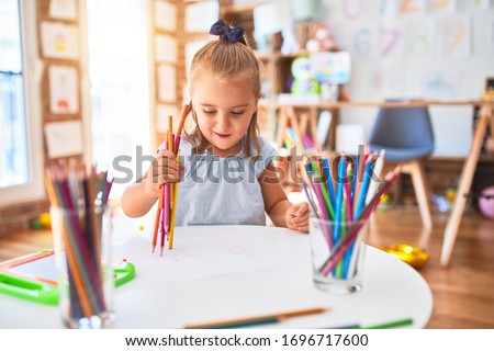 Young beautiful blonde girl kid enjoying play school with toys at kindergarten, smiling happy painting with pencil colors at home Royalty-Free Stock Photo #1696717600