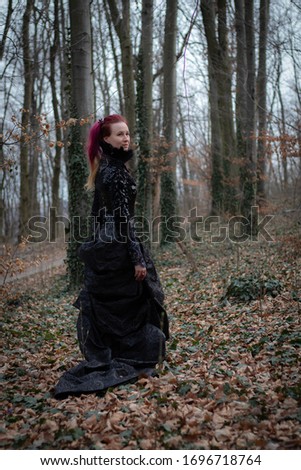 portrait of a woman with red hair and in a black long beautiful dress in the forest among the trees entwined with ivy