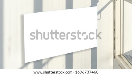 large blank poster with space for design hangs on white wall near glass door in public hallway on sunny day