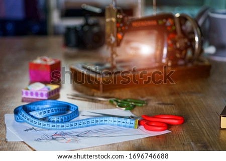 Blue measuring tape and scissors with red handle on sketches with dresses. Tailor`s sketches, design work. Draft with beautiful dresses on table. Tailor concept. Close-up.