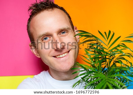 young guy man in a white T-shirt, colorful background, decorative palm, emotions photo, home plant, love of nature