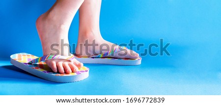 Closeup child feet wearing a pair of fun bright flip-flops on blue background. Kids and family lifestyle outdoors. The concept of children's and family vacations in the water or summer holidays. Royalty-Free Stock Photo #1696772839