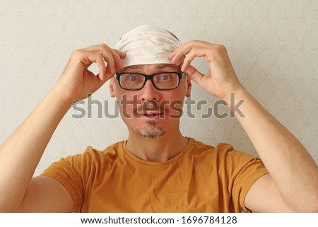 Young man incorrectly puts disposable protective white medical hygiene mask on his forehead to protect himself from respiratory, infectious viral diseases, from coronavirus. Humor, positive, fool. Royalty-Free Stock Photo #1696784128