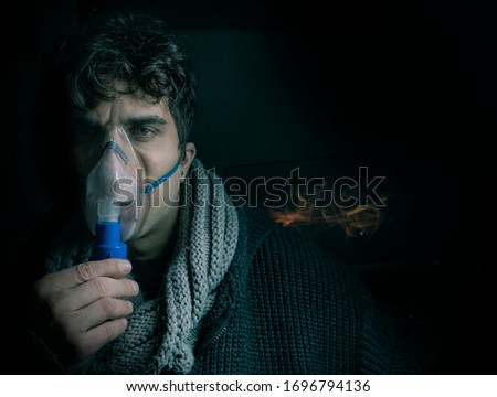 Dark Portrait of man using steam vapor inhaler nebulizer doing aerosol inhalation medicine treatment at home or hospital flu and asthma bronchitis virus healing.  Royalty-Free Stock Photo #1696794136