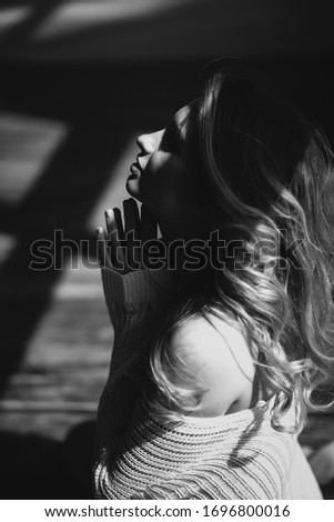 A beautiful woman with curly hair sits on the floor in the sunshine folded her hands in prayer to God. Black and white art photo. Soft selective focus.