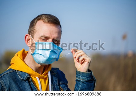 Close up portrait of a man outdoor in a surgical mask with rubber ear straps. Typical three-layer surgical mask for covering the mouth and nose. Bacteria mask procedure. Protection concept.