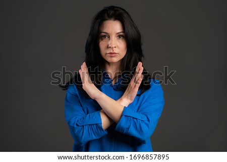 Mature woman disapproving with no crossing hands sign make negation gesture. Denying, Rejecting, Disagree, Portrait of pretty lady on grey background.