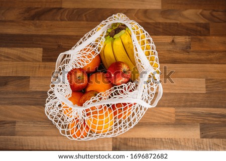 Top view of a woman taking photos with the smartphone of fruits and vegetables in a reusable organic cotton mesh bag. Zero waste, plastic free concept. Sustainable lifestyle.