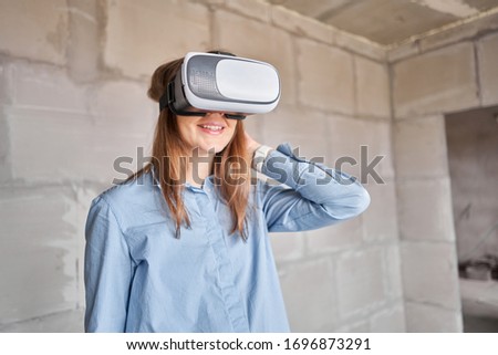 Woman architect or construction engineer wear virtual reality glasses inside a building site. Concrete walls in new apartment, concept of repair.