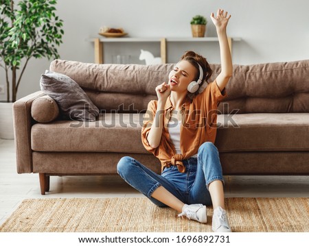 Young female in casual outfit listening to music in headphones and singing while sitting on floor near sofa and having fun at home
 Royalty-Free Stock Photo #1696892731