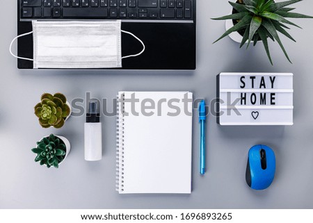 Light box with text STAY HOME, laptop, notepad, medicine mask and sanitizer spray on gray background. Coronavirus, Quarantine and isolation concept. Covid-19, 2019-nCoV. Top view.