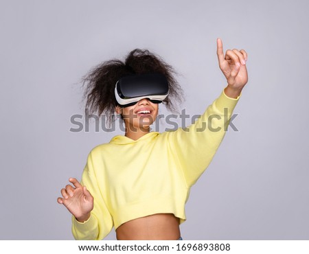 Smiling girl interacting with invisible screen while having virtual reality experience on grey background