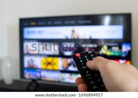 Tv remote controller in hand of customer looking for some content in Smart Tv app for streaming video. Watching streaming services for entertainment on television. Choosing TV series and movies Royalty-Free Stock Photo #1696894957