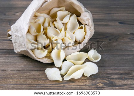 Pouch bag with pasta conchiglie flatlay, top view. Packaging on dark wooden background. Italian conchiglie or durum wheat shells.
