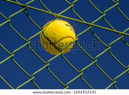 Yellow Tennis Ball Stuck In Green Fence Royalty-Free Stock Photo #1696922545