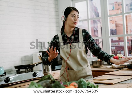 Picture of young amazing emotional woman dancing in kitchen indoors at home listening music with headphones cooking. fresh vegetables putting on wooden counter table. lady in earphones moving body