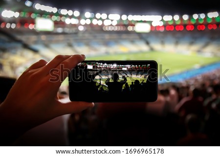 Taking pictures on a mobile phone in a sports stadium. Focused on fans