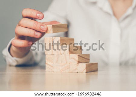 Business investment concept - hand builds a ladder from wooden blocks. Close up. Royalty-Free Stock Photo #1696982446