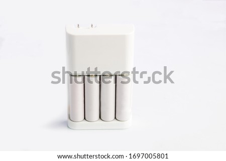 A set of white long lasting rechargeable AA batteries and compatible  outlet charger on white background.
