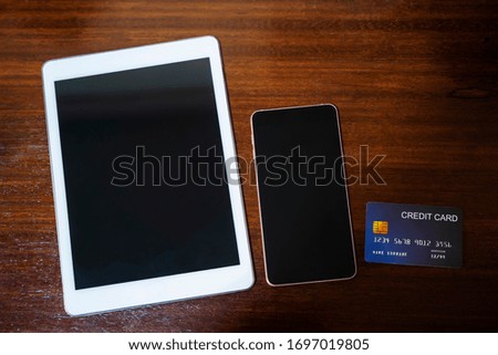 Tablet, mobile with empty screen and credit card on wood table. Shopping online and technology concept.